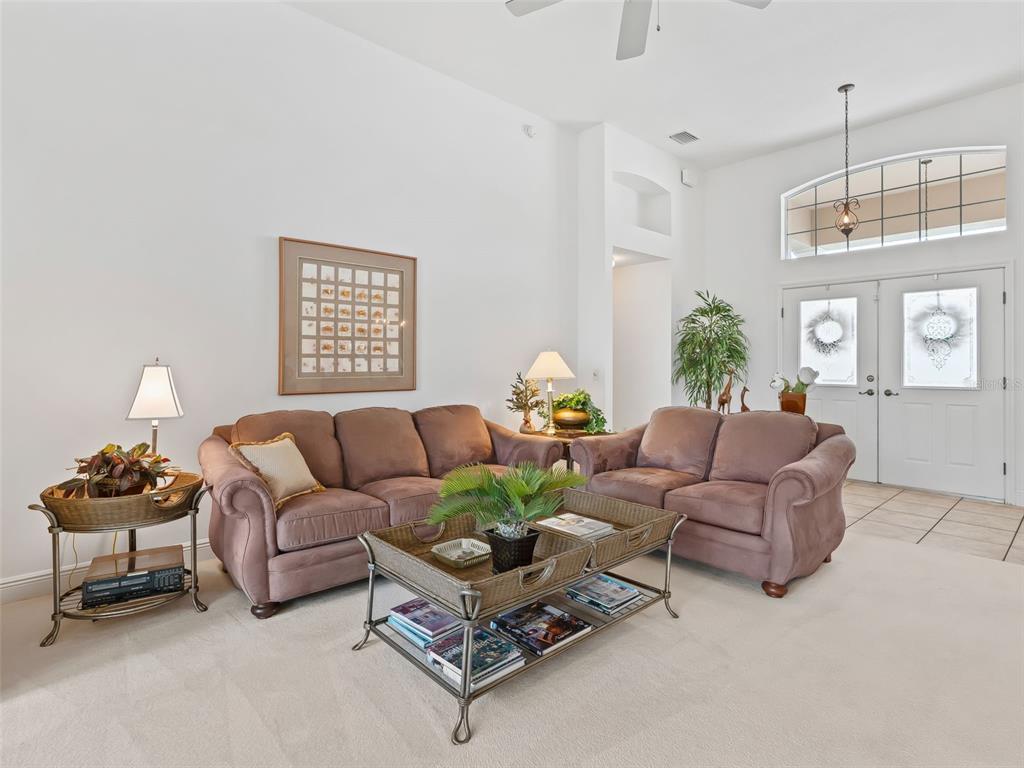 A living room features two brown sofas, a wicker coffee table, and a high ceiling — 8755 SE 177TH GRASSMERE STREET, THE VILLAGES, FL