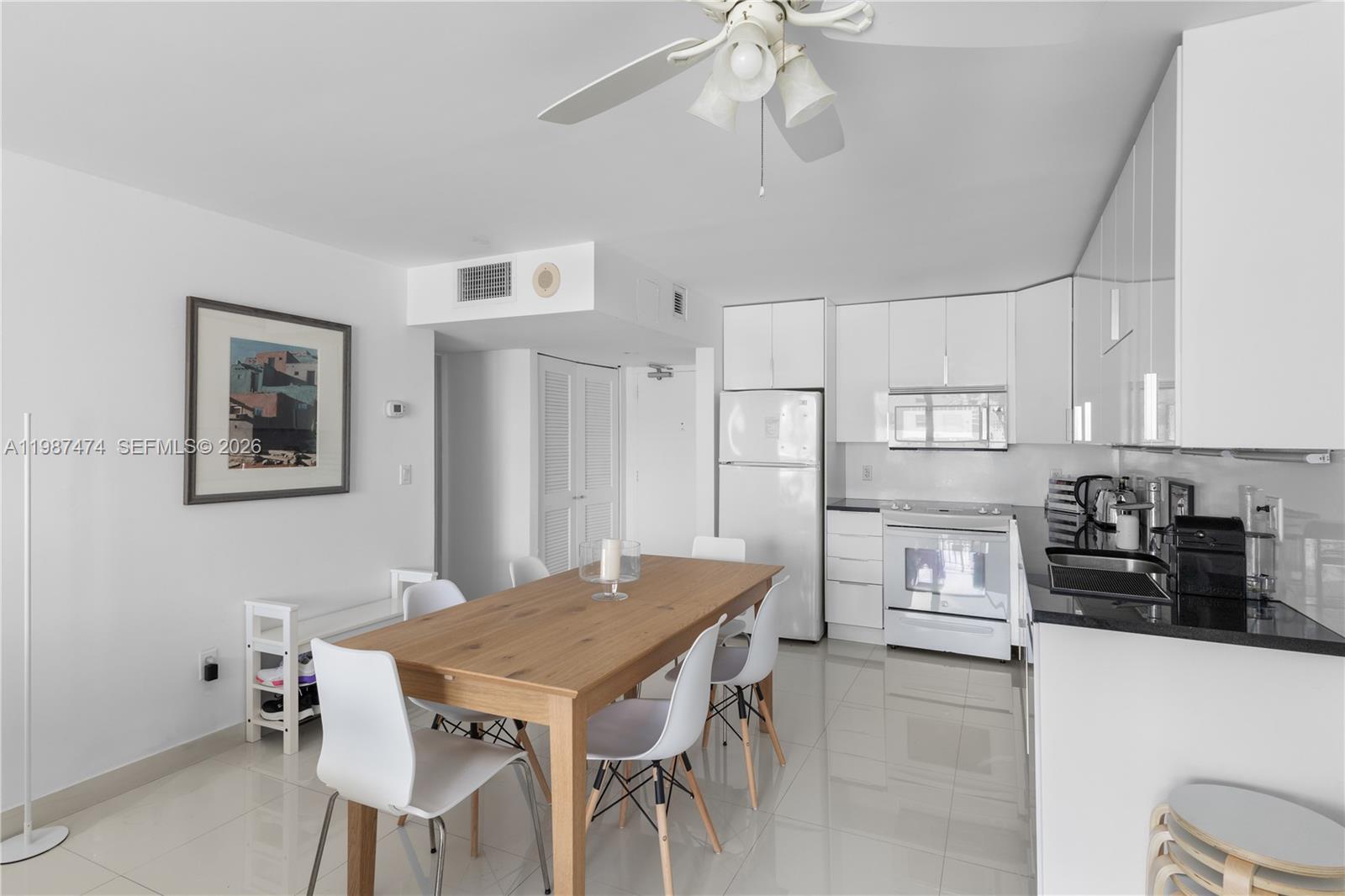 A dining area with a wooden table and white chairs sits adjacent to a kitchen — 345 Ocean Dr # 607, Miami Beach FL 33139, MIAMI BEACH, FL