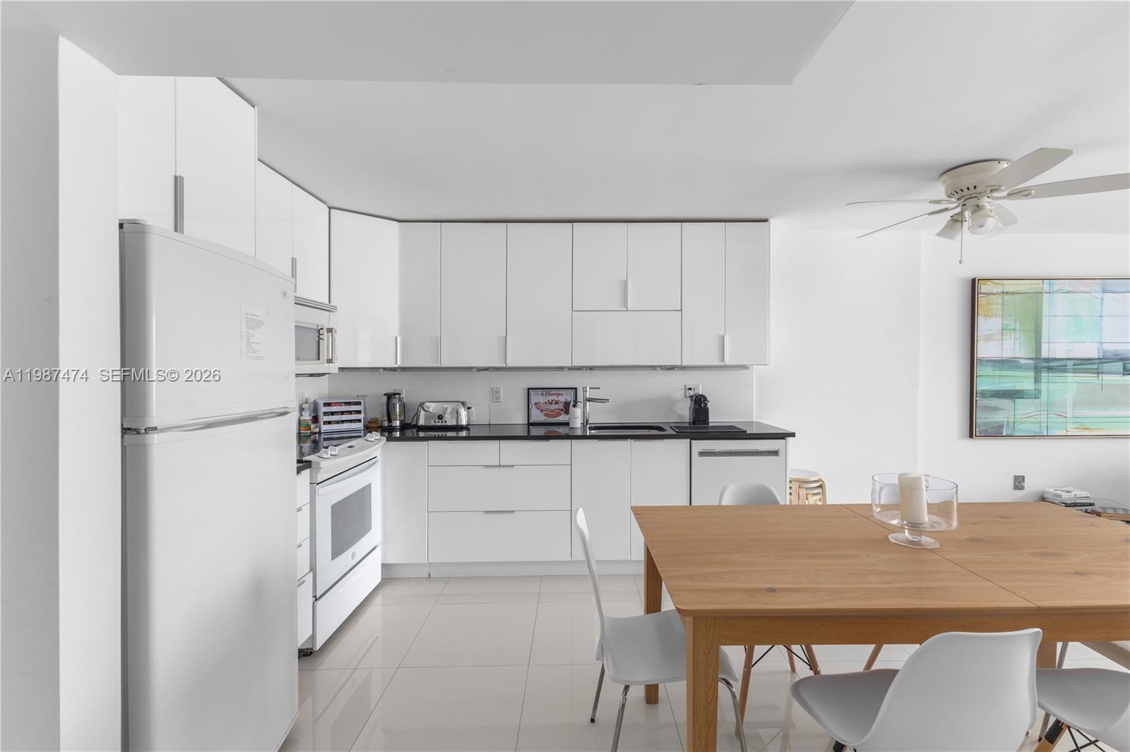 A modern kitchen features white cabinets, black countertops, and a dining table in the foreground — 345 Ocean Dr # 607, Miami Beach FL 33139, MIAMI BEACH, FL