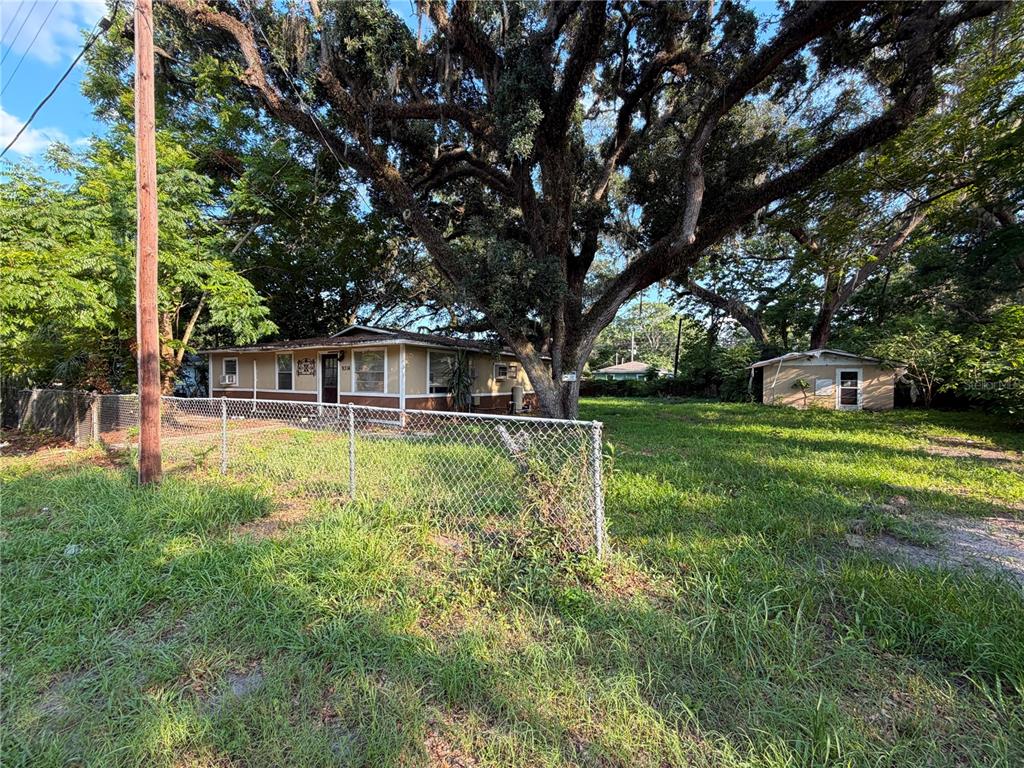 A single-story house with a detached shed sits on a grassy lot under large trees — 9314 MANGO STREET, NEW PORT RICHEY, FL