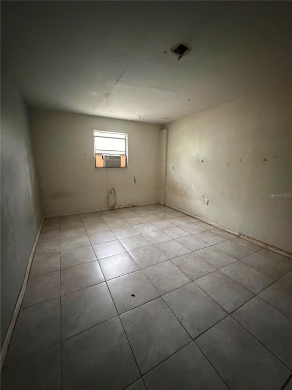 An empty room features light-colored floor tiles, white walls, and a window with an air conditioner — 9314 MANGO STREET, NEW PORT RICHEY, FL