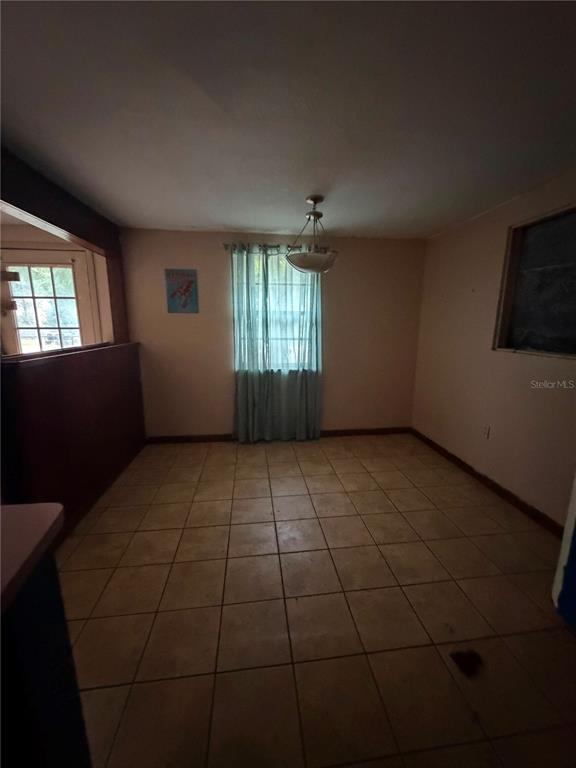 A dining room with light-colored floor tiles, a central pendant light, and a window with curtains — 9314 MANGO STREET, NEW PORT RICHEY, FL