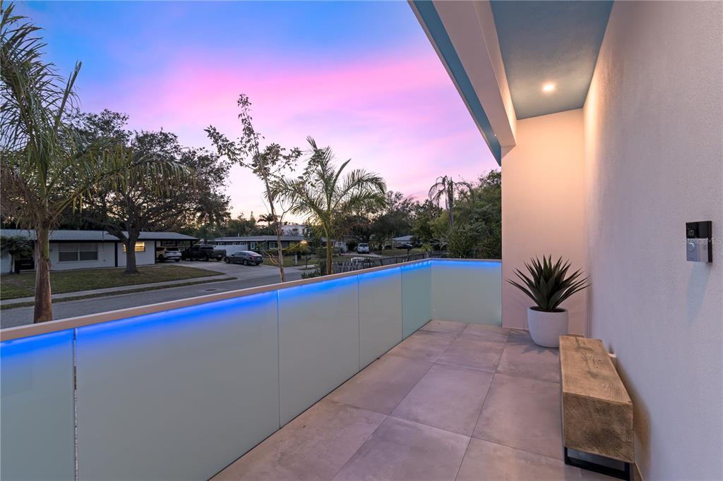 A modern balcony features frosted glass railings with blue LED lighting and tiled flooring — 2585 CLEMATIS STREET, SARASOTA, FL