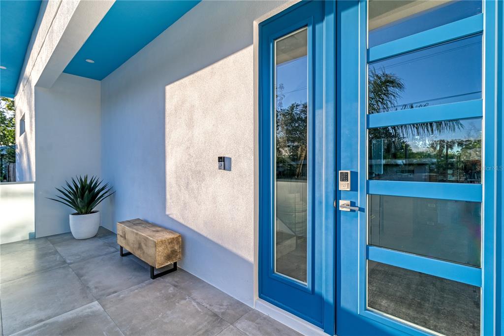 A bright blue front door with glass panels sits next to a bench and plant — 2585 CLEMATIS STREET, SARASOTA, FL