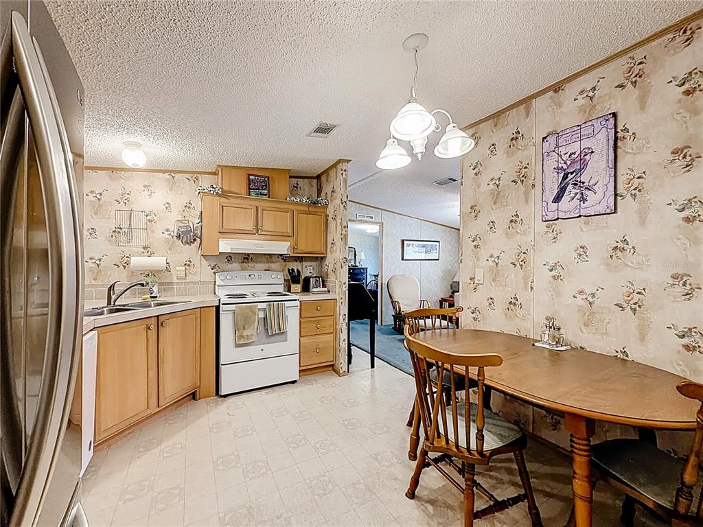 A kitchen and dining area with light wood cabinets, floral wallpaper, and a wooden table — 18845 SE 18TH PLACE, SILVER SPRINGS, FL