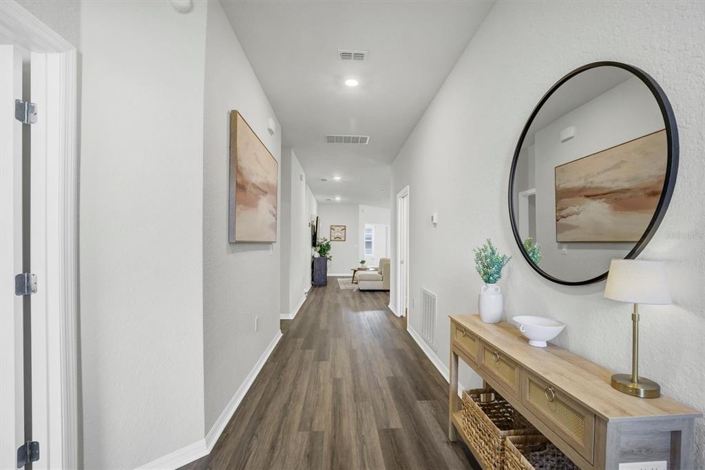 A hallway with wood-look flooring leads to a living area, featuring a console table and mirror — 4519 RAPALLO AVENUE, WINTER HAVEN, FL