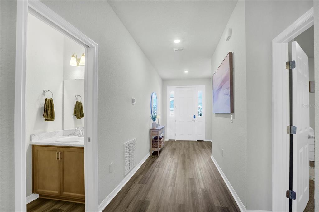 A hallway with wood-look flooring leads to a front door, with a bathroom on the left — 4519 RAPALLO AVENUE, WINTER HAVEN, FL