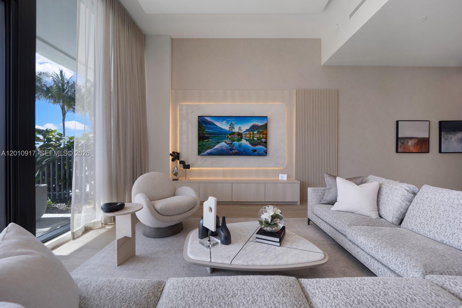 A modern living room features a large sectional sofa, floor-to-ceiling windows, and outdoor patio views — 900 N Ocean Blvd # 106, Pompano Beach FL 33062, POMPANO BEACH, FL