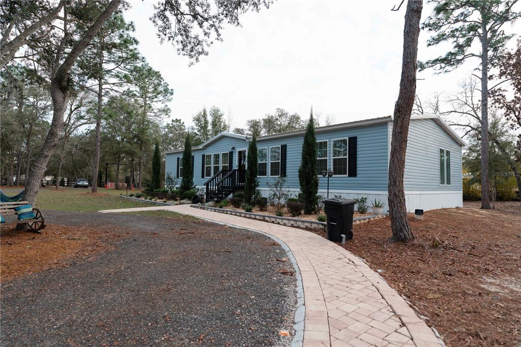 A light blue manufactured home sits on a wooded lot with a paved walkway — 7670 NE 97TH COURT, BRONSON, FL