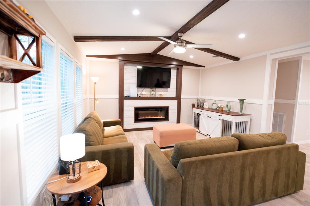 A living room features a fireplace, a television, two sofas, and exposed ceiling beams — 7670 NE 97TH COURT, BRONSON, FL