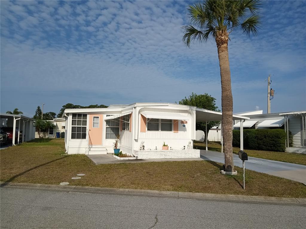 A single-story mobile home with white siding, peach shutters, and a carport under a palm tree — 5119 GLEN ECHO AVENUE, SARASOTA, FL