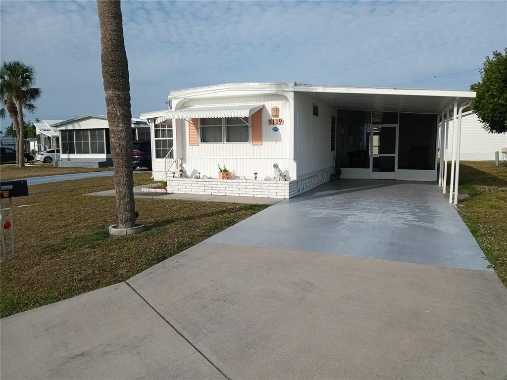 A single-story manufactured home features a white exterior, a carport, and a small brick planter — 5119 GLEN ECHO AVENUE, SARASOTA, FL