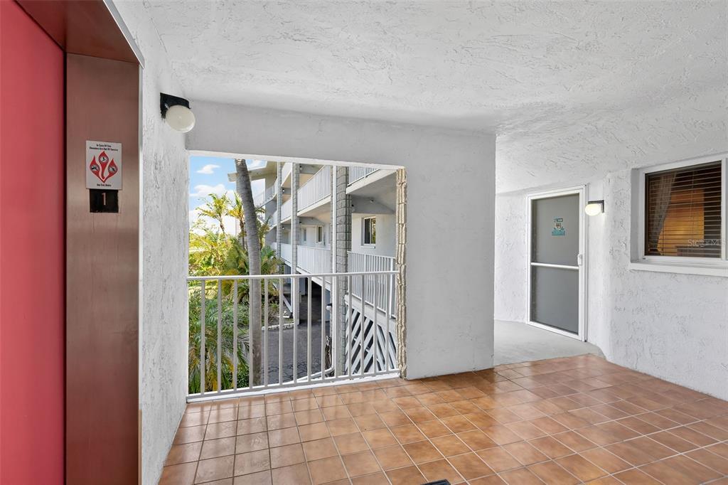 An outdoor tiled walkway features an elevator, a metal railing, and a screen door entrance — 1401 S MCCALL ROAD UNIT 104B, ENGLEWOOD, FL