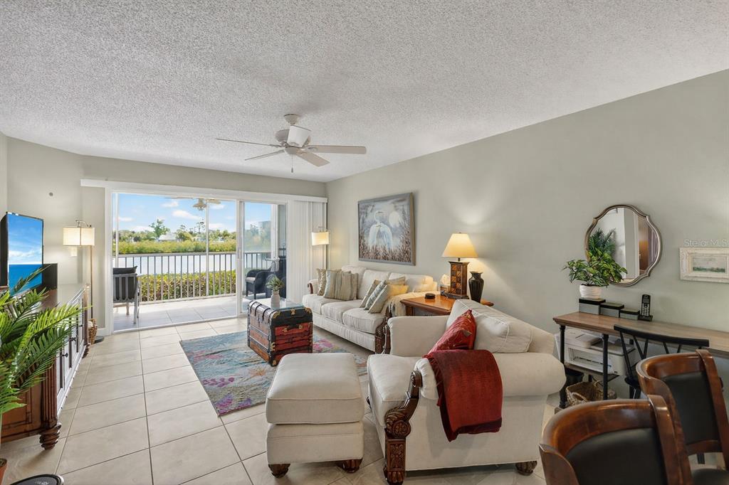 A living room features light tile floors, a white sofa, and a sliding glass door balcony — 1401 S MCCALL ROAD UNIT 104B, ENGLEWOOD, FL