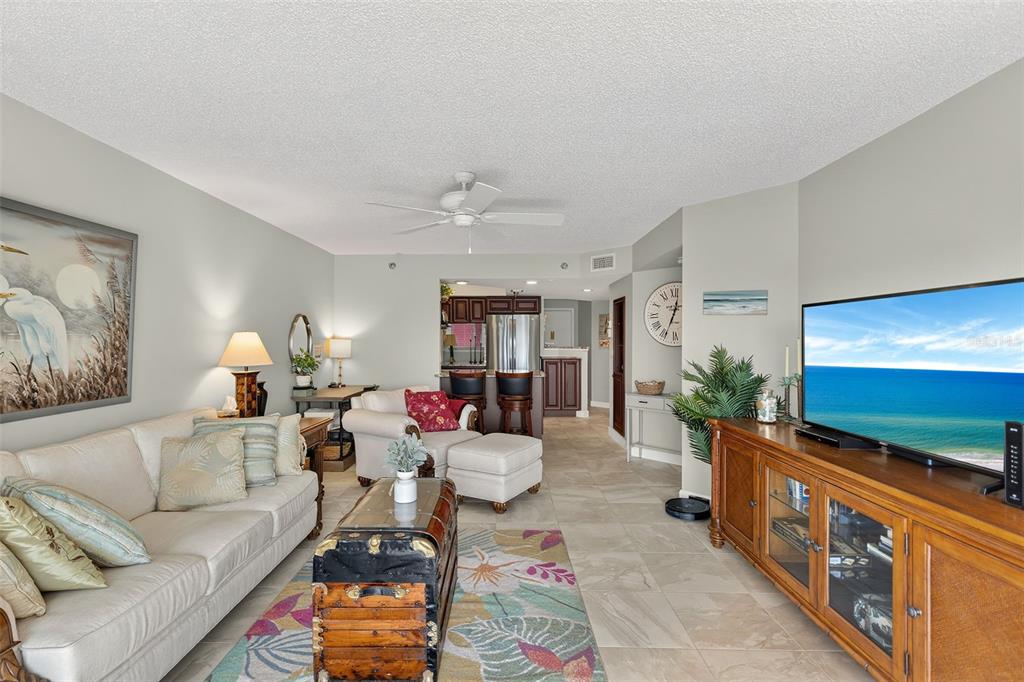 A living room with a beige sofa, patterned rug, wooden media console, and kitchen view — 1401 S MCCALL ROAD UNIT 104B, ENGLEWOOD, FL