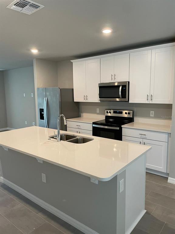 A kitchen features a white island with a sink, white cabinets, and stainless steel appliances — 17177 CAGAN CROSSINGS BOULEVARD, CLERMONT, FL