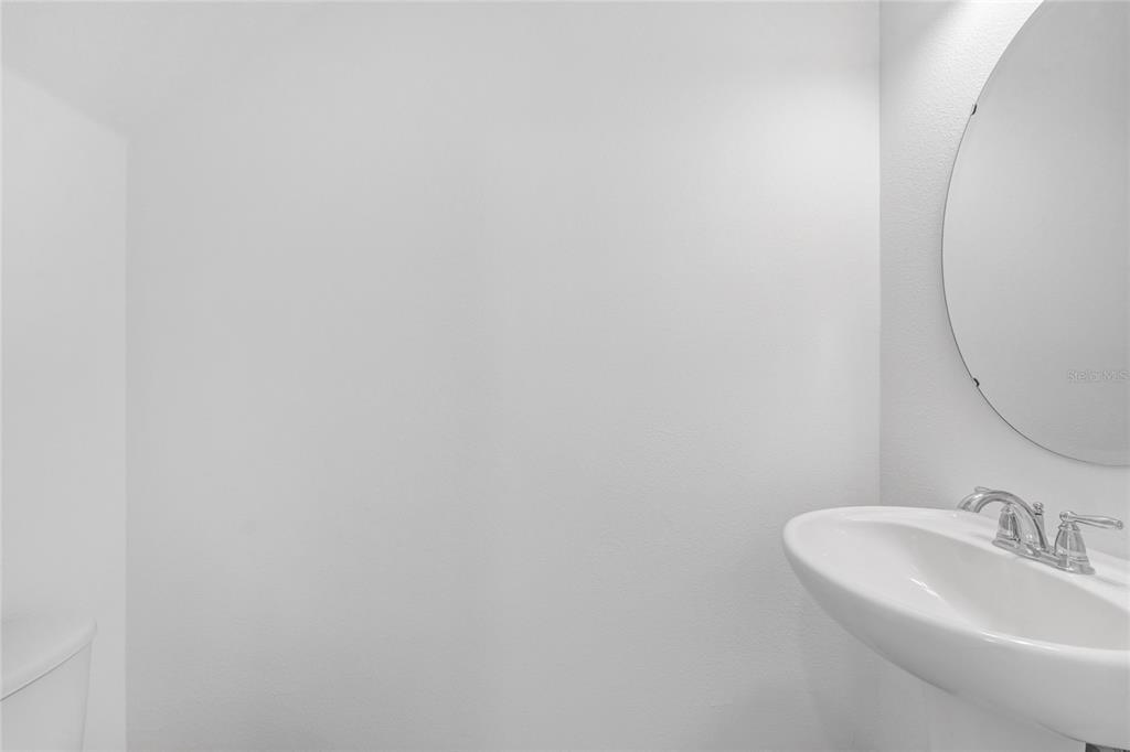 A white pedestal sink and a round mirror are mounted on a plain white wall — 763 LONGBOAT DRIVE, DAVENPORT, FL