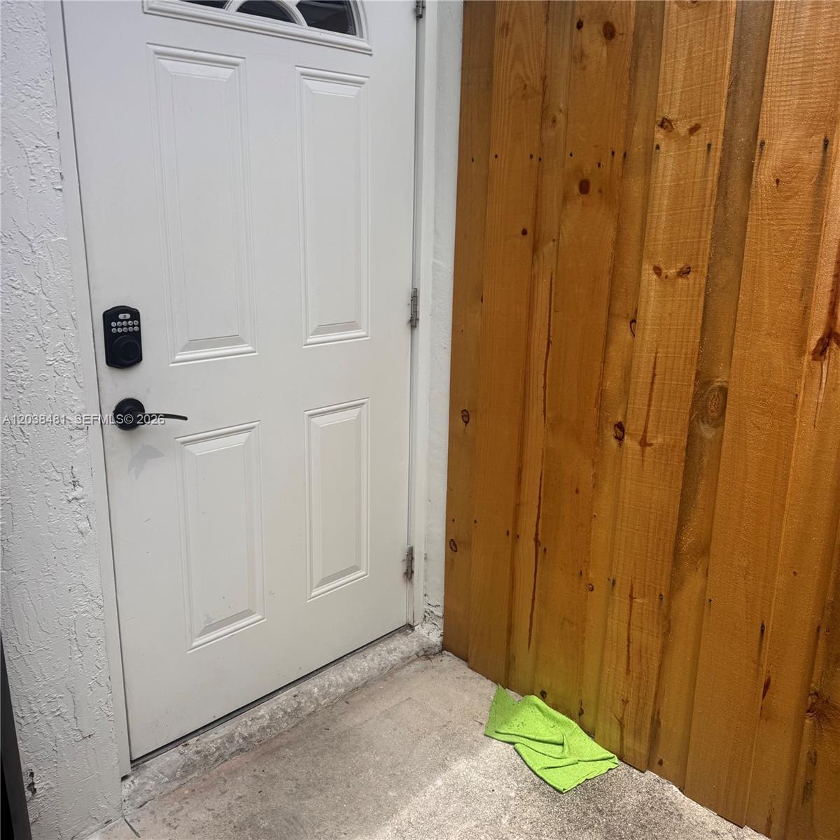 A white door with a keypad lock stands next to a wooden privacy fence — MIAMI, FL