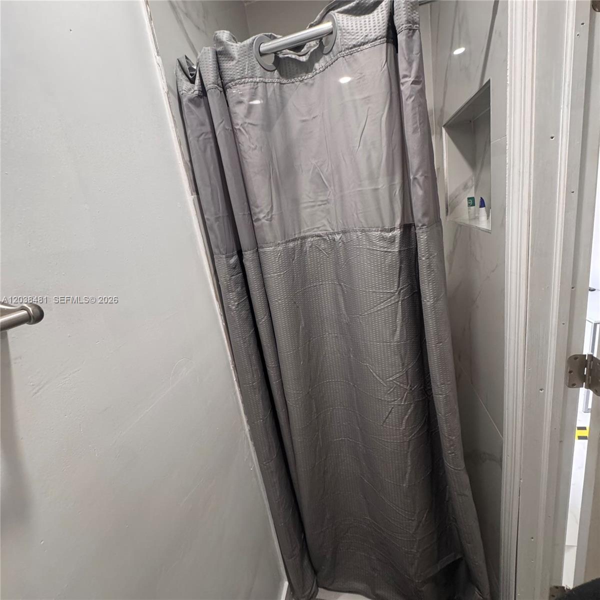 A gray shower curtain hangs in a bathroom with marble-tiled walls and a recessed niche — MIAMI, FL