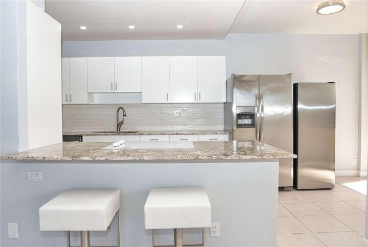 A modern kitchen features white cabinets, stainless steel appliances, and a granite-topped breakfast bar — 19355 Turnberry Way # 3d, Miami FL 33180, MIAMI, FL