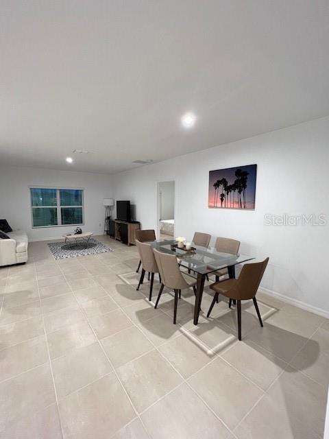 This open-concept dining and living area features light tile flooring and a glass-top table — 200 AQUAMARINE LANE, KISSIMMEE, FL