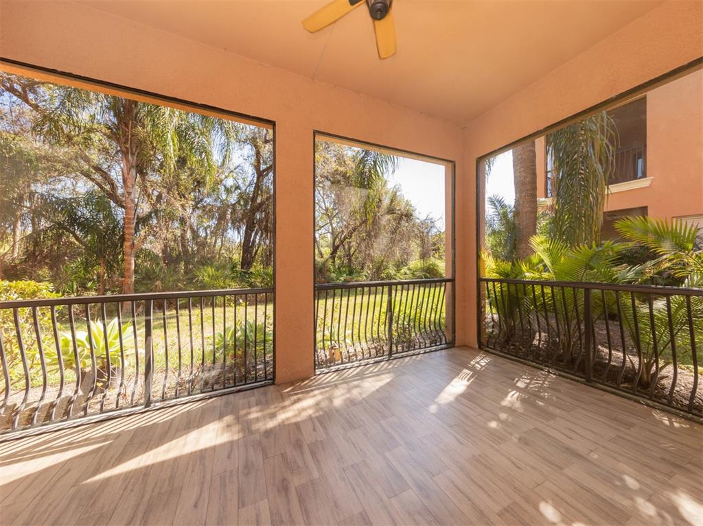 A screened-in porch with wood-look tile flooring, a ceiling fan, and views of trees — 5531 46TH COURT W UNIT 5531, BRADENTON, FL