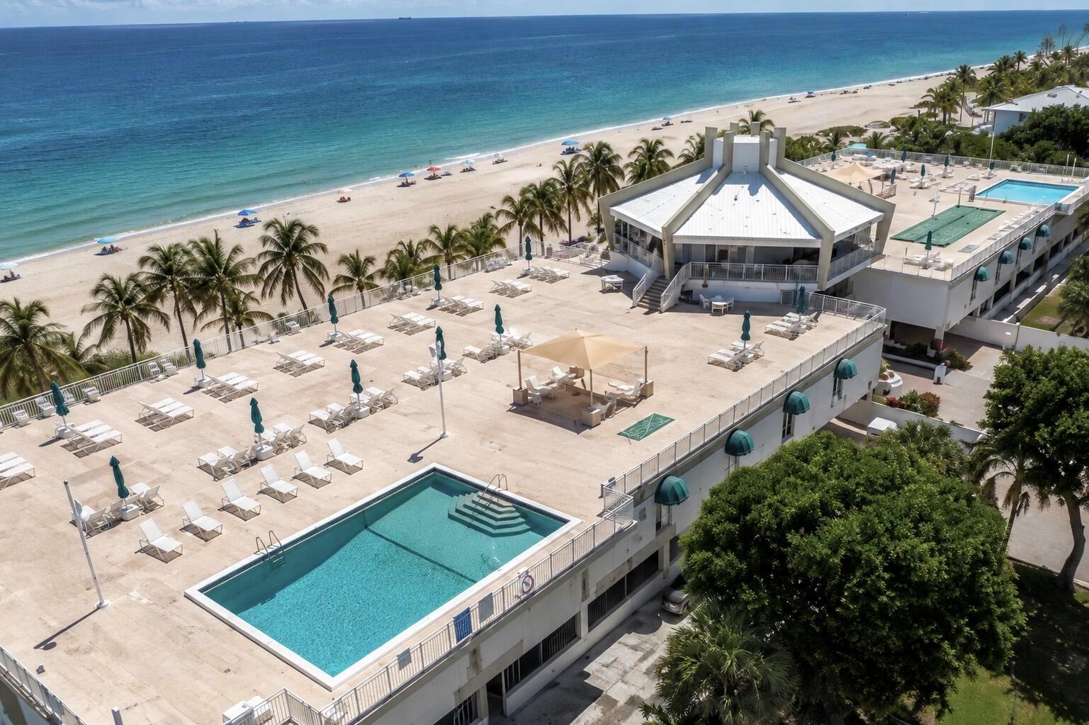 An aerial view of a hotel rooftop featuring a swimming pool, lounge chairs, and beach access — 111 Briny Avenue # 12, Pompano Beach FL 33062, POMPANO BEACH, FL