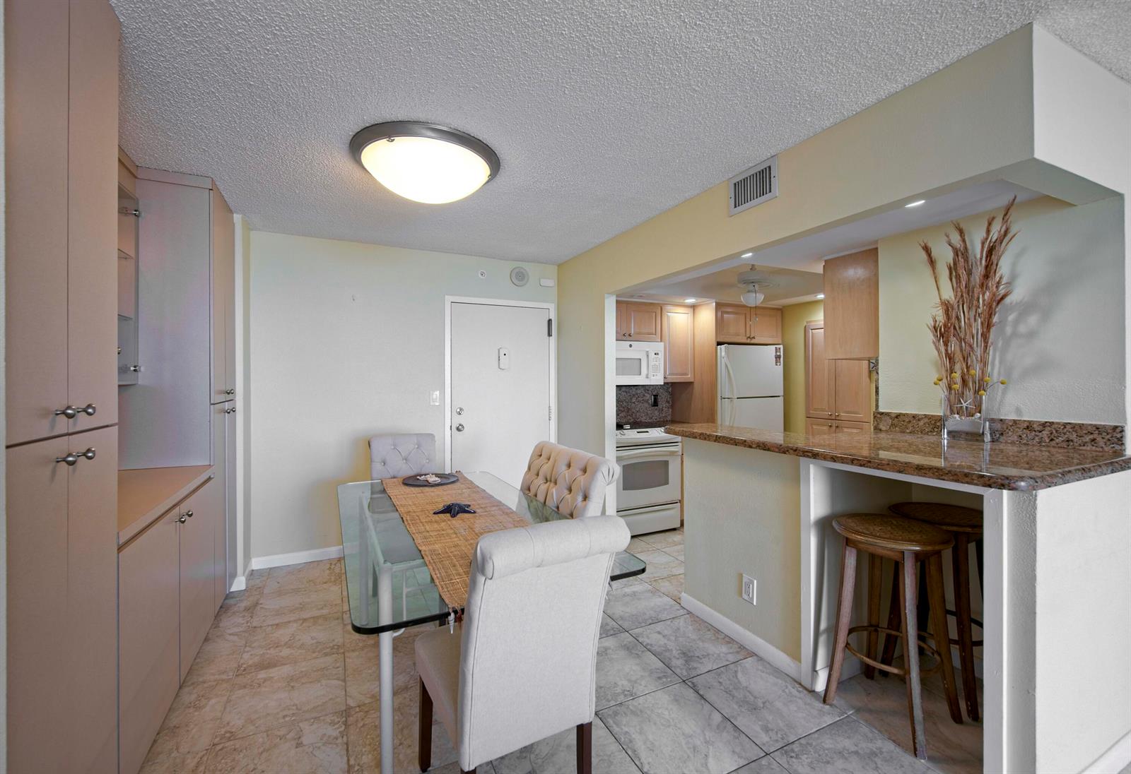 A dining area with a glass table and chairs next to a kitchen with bar seating — 111 Briny Avenue # 12, Pompano Beach FL 33062, POMPANO BEACH, FL