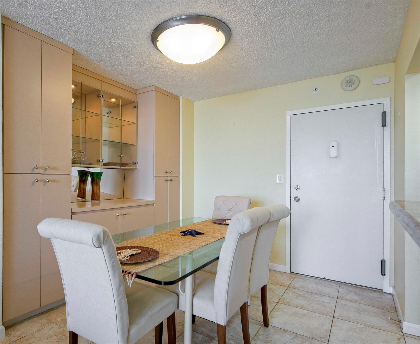 A dining area features a glass table, upholstered chairs, built-in cabinetry, and tile flooring — 111 Briny Avenue # 12, Pompano Beach FL 33062, POMPANO BEACH, FL