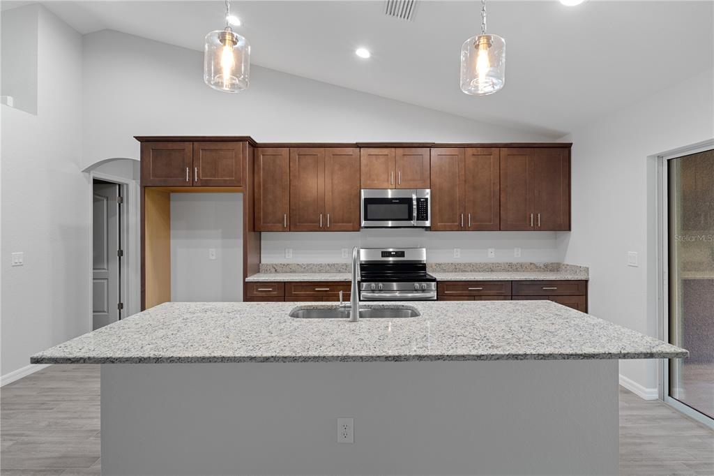 A kitchen features dark wood cabinets, granite countertops, a central island, and stainless steel appliances — 4118 N PINK POPPY DRIVE, BEVERLY HILLS, FL