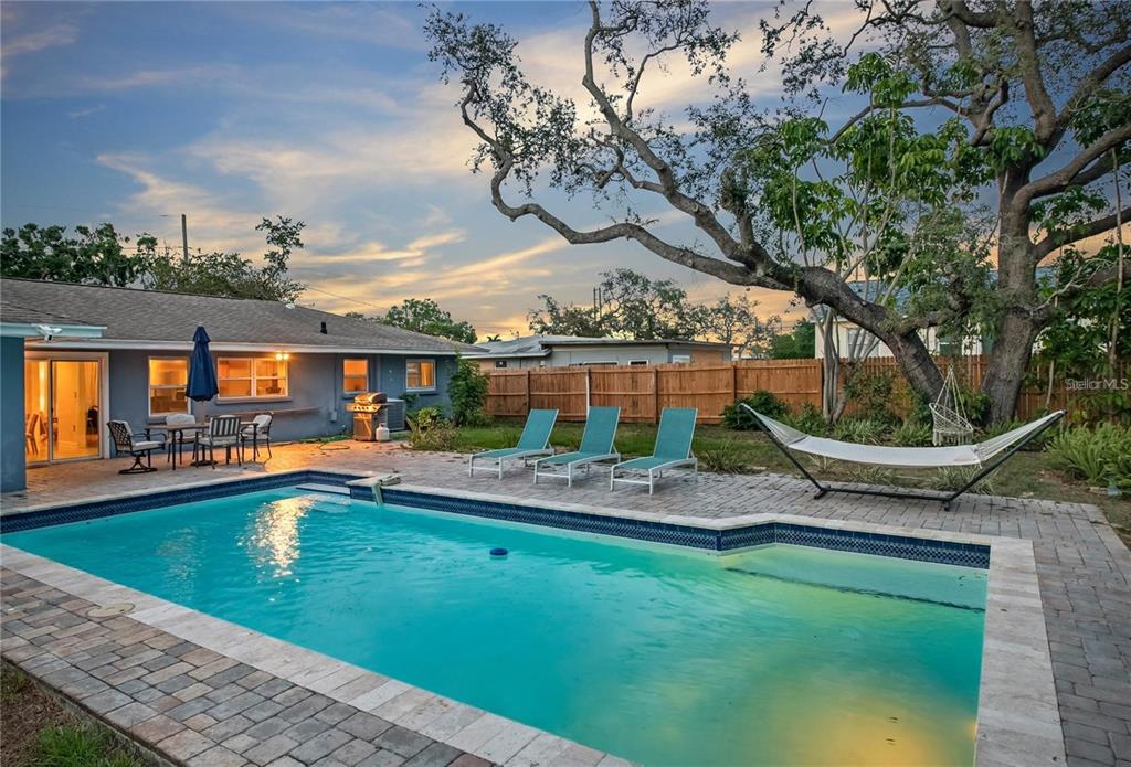 A backyard features a rectangular swimming pool, a brick patio, lounge chairs, and a hammock — 14626 WILDWOOD DRIVE, LARGO, FL