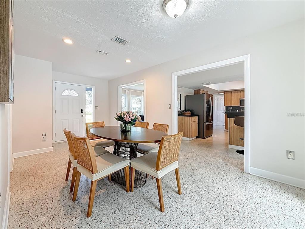 A dining area with a round table and chairs features light-colored walls and speckled flooring — 14626 WILDWOOD DRIVE, LARGO, FL
