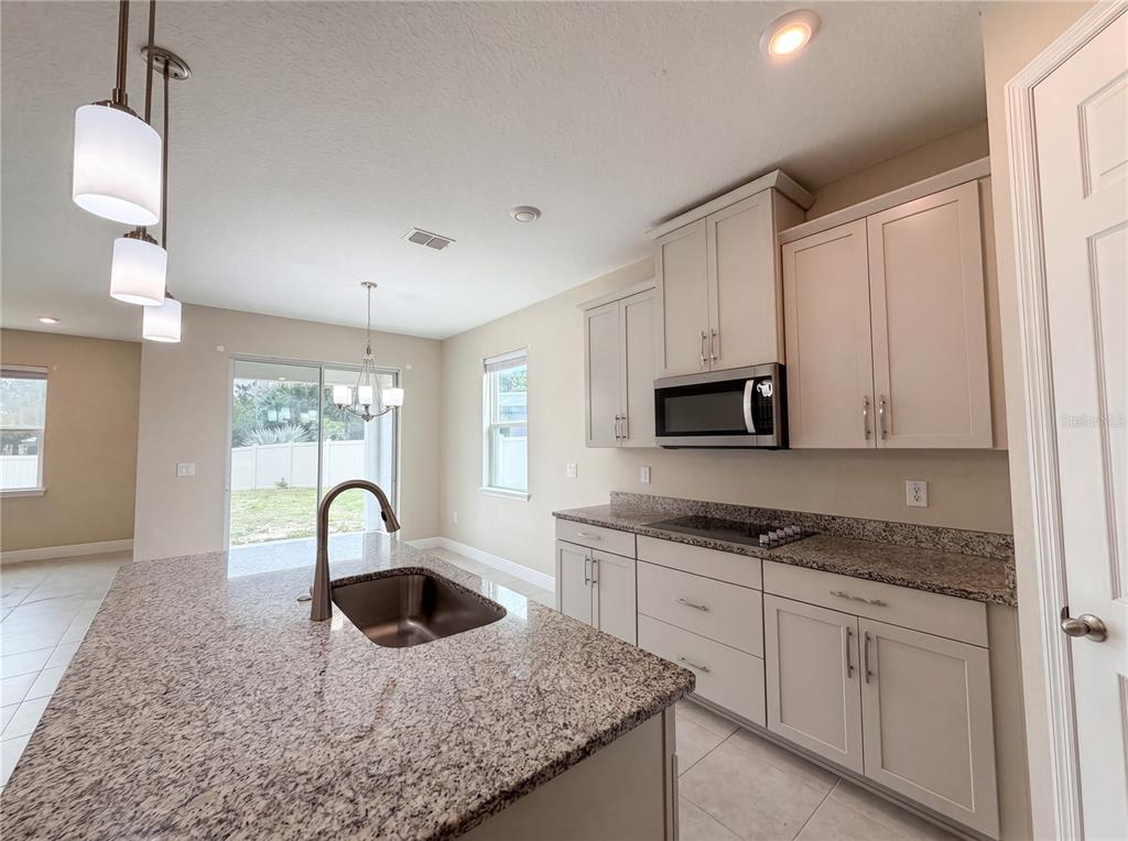 A kitchen features granite countertops, light-colored cabinetry, a center island with a sink, and appliances — 528 BELLISSIMO PLACE, HOWEY IN THE HILLS, FL