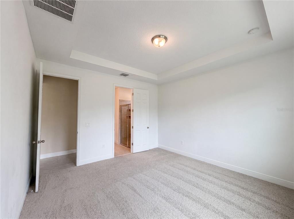 A bedroom with beige carpet, white walls, a tray ceiling, and two open doorways — 528 BELLISSIMO PLACE, HOWEY IN THE HILLS, FL