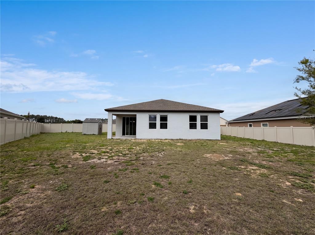 A white house with a covered patio and a large, grassy backyard enclosed by fencing — 528 BELLISSIMO PLACE, HOWEY IN THE HILLS, FL