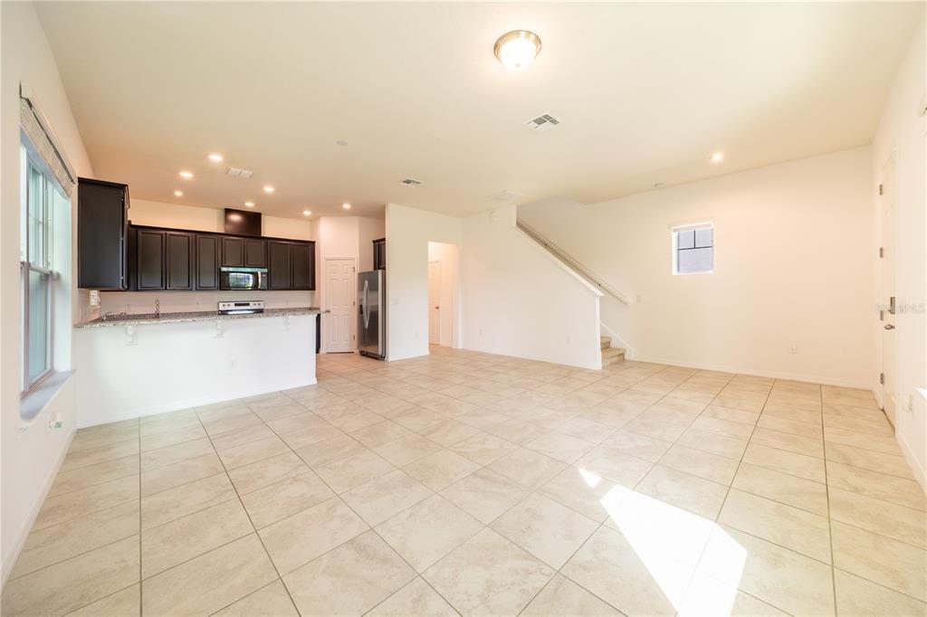 An open-concept kitchen with dark cabinets and a large tiled living area with stairs — 2247 WHITE FEATHER LOOP, OAKLAND, FL