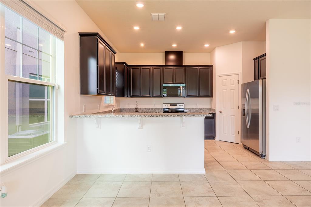 A kitchen features dark wood cabinets, granite countertops, stainless steel appliances, and tile flooring — 2247 WHITE FEATHER LOOP, OAKLAND, FL