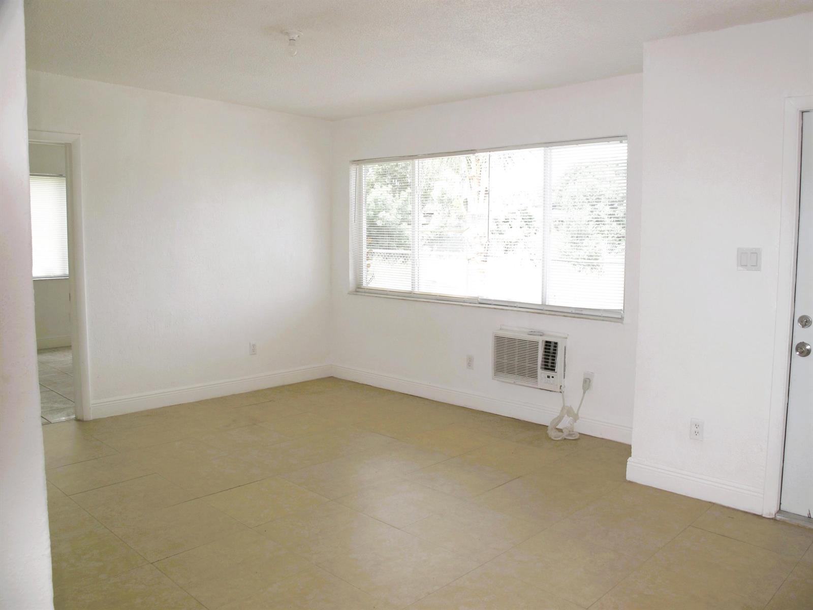 An empty room with white walls, tile flooring, a large window, and a wall air conditioner — 340 NW 6th Street # 2, Pompano Beach FL 33060, POMPANO BEACH, FL