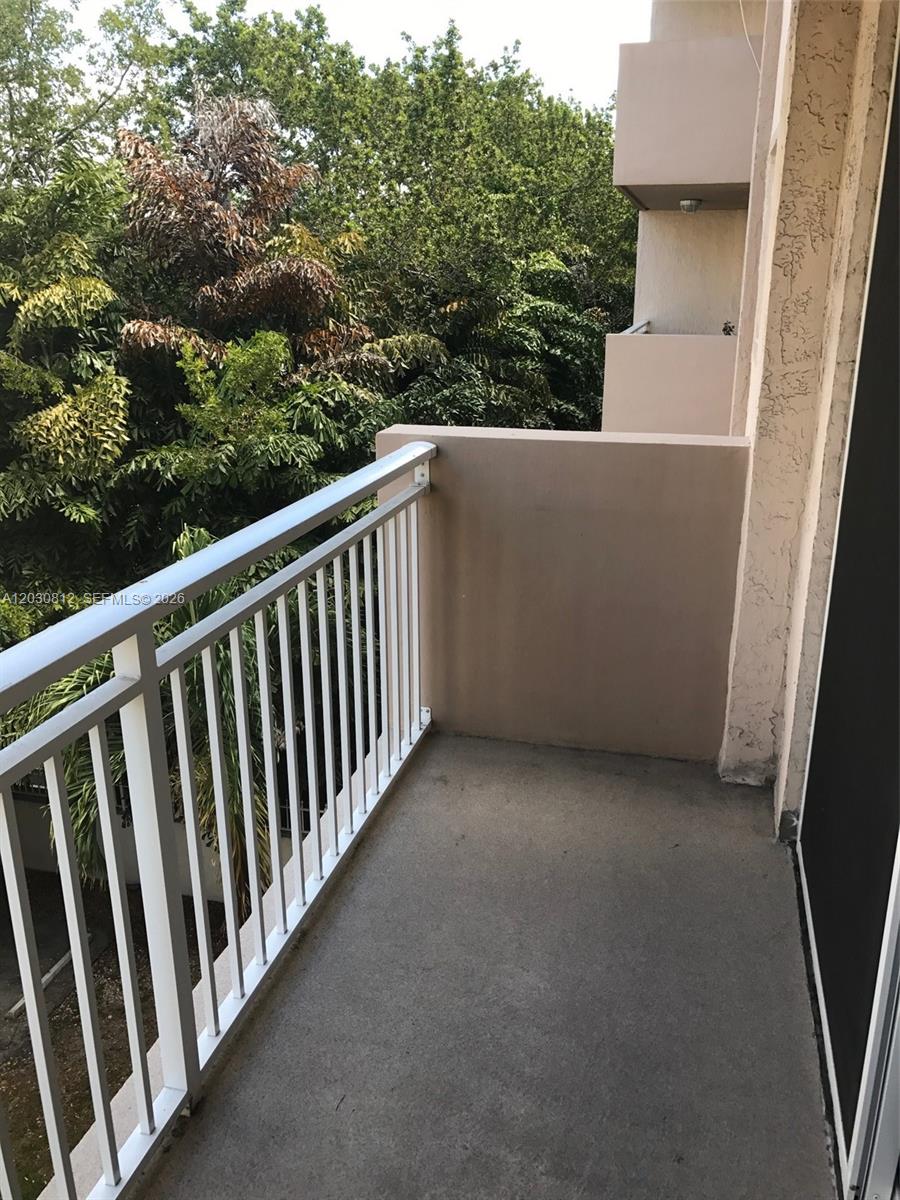 A concrete balcony features a white metal railing overlooking a view of dense green trees — 1665 Bay Rd # 416, Miami Beach FL 33139, MIAMI BEACH, FL