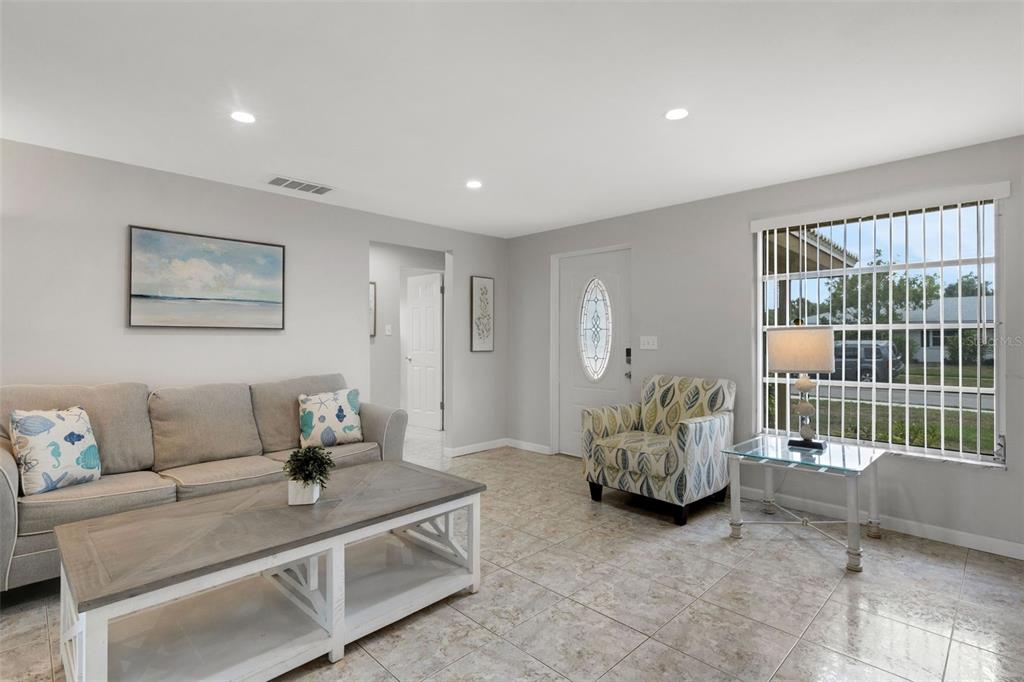 A living room features light gray walls, tile flooring, a gray sofa, and a patterned armchair — 3174 REGATTA CIRCLE, SARASOTA, FL
