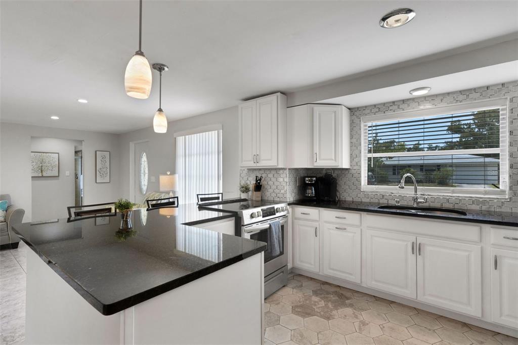 A kitchen features white cabinets, black countertops, a tiled backsplash, and a hexagonal tile floor — 3174 REGATTA CIRCLE, SARASOTA, FL