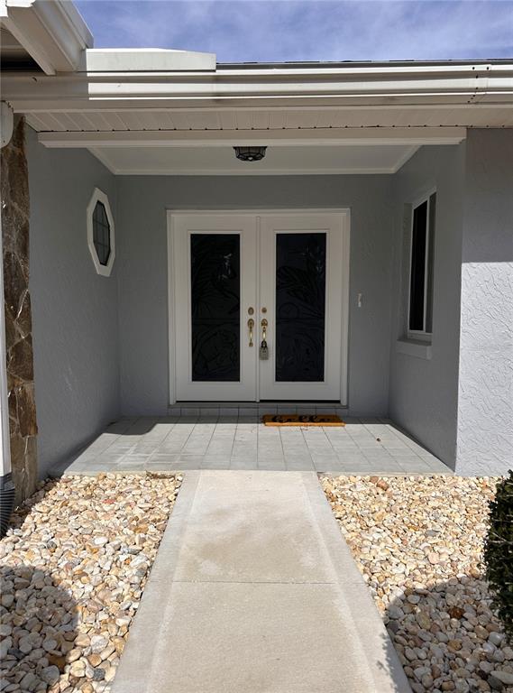 A concrete walkway leads to a covered entryway with double glass-paneled doors — 100 WEBSTER LANE, PALM COAST, FL