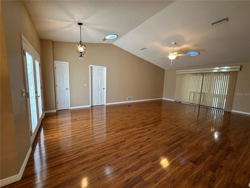 An empty room features hardwood floors, a vaulted ceiling with skylights, and sliding glass doors — 100 WEBSTER LANE, PALM COAST, FL