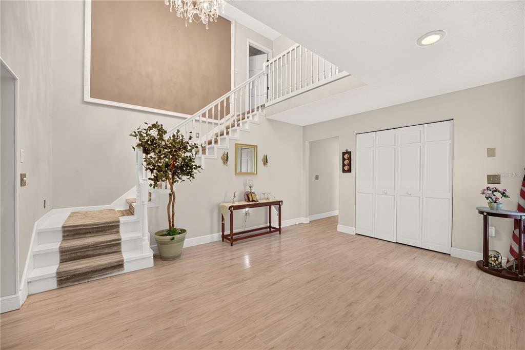 A bright foyer features light wood flooring, a staircase with a runner, and white closet doors — 5360 NE 1ST LANE, OCALA, FL
