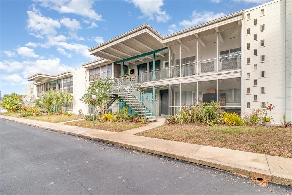 A two-story apartment building features screened-in balconies, an exterior staircase, and a decorative concrete block wall — 151 N ORLANDO AVENUE UNIT 207, WINTER PARK, FL
