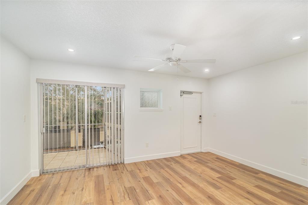 An empty room features wood-look flooring, a ceiling fan, a sliding glass door, and a door — 151 N ORLANDO AVENUE UNIT 207, WINTER PARK, FL