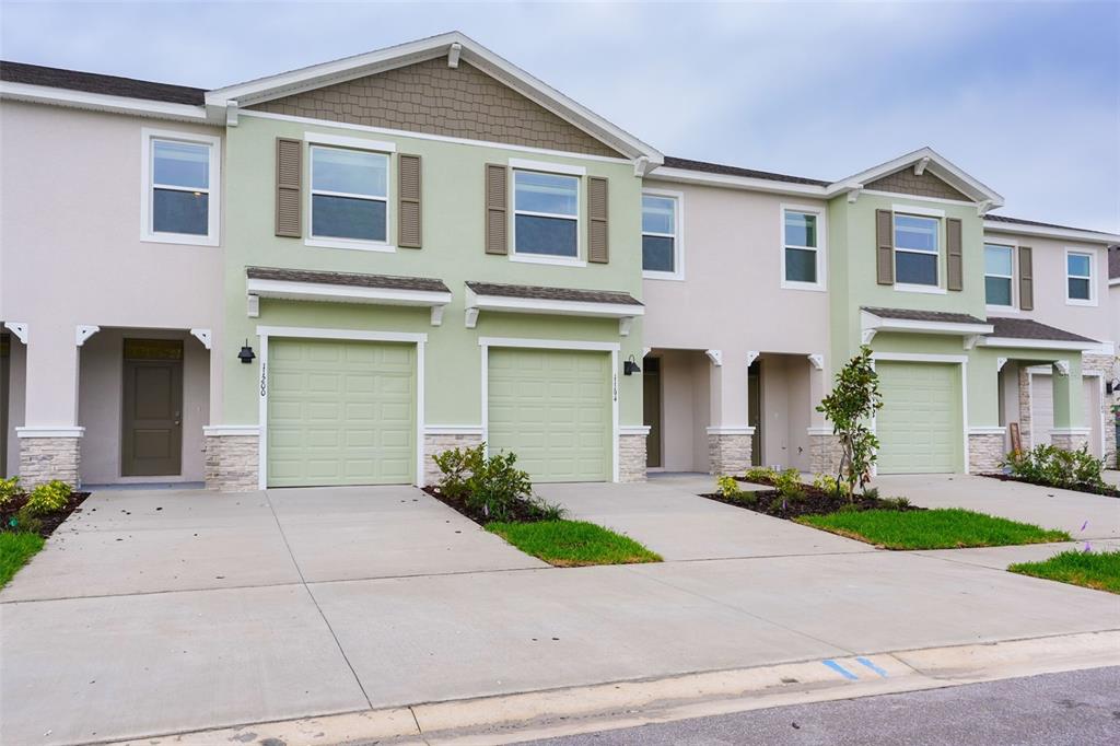 A row of multi-story townhomes with light green and beige siding, garages, and concrete driveways — 11194 TREASURE SWALE WAY, LAND O LAKES, FL