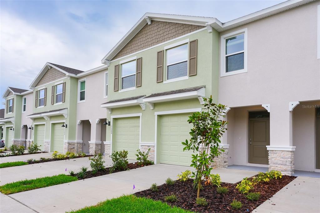 A row of multi-story townhomes with light green and beige stucco facades and stone accents — 11194 TREASURE SWALE WAY, LAND O LAKES, FL