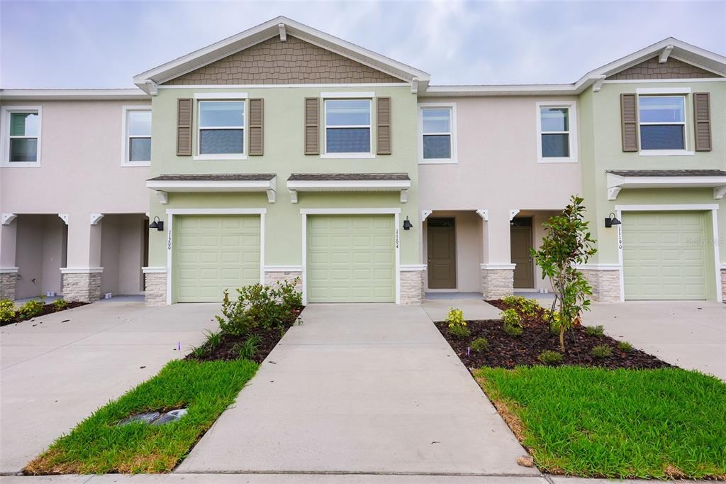 A row of three-story townhomes with light green garages, beige stucco walls, and stone accents — 11194 TREASURE SWALE WAY, LAND O LAKES, FL