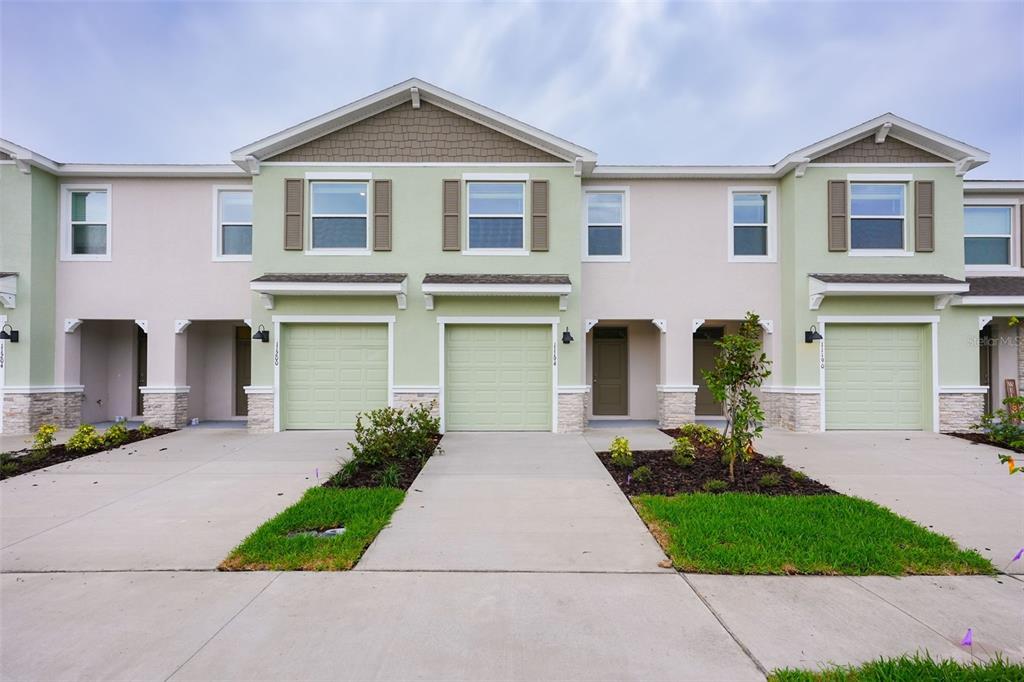 A row of three attached townhomes features light green garages, beige stucco walls, and stone accents — 11194 TREASURE SWALE WAY, LAND O LAKES, FL